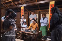 Los visitantes observan a un calígrafo realizar una demostración de caligrafía en un espacio de cultura tradicional durante el recorrido nocturno por el Templo de la Literatura en Hanoi. (Foto: VNA)